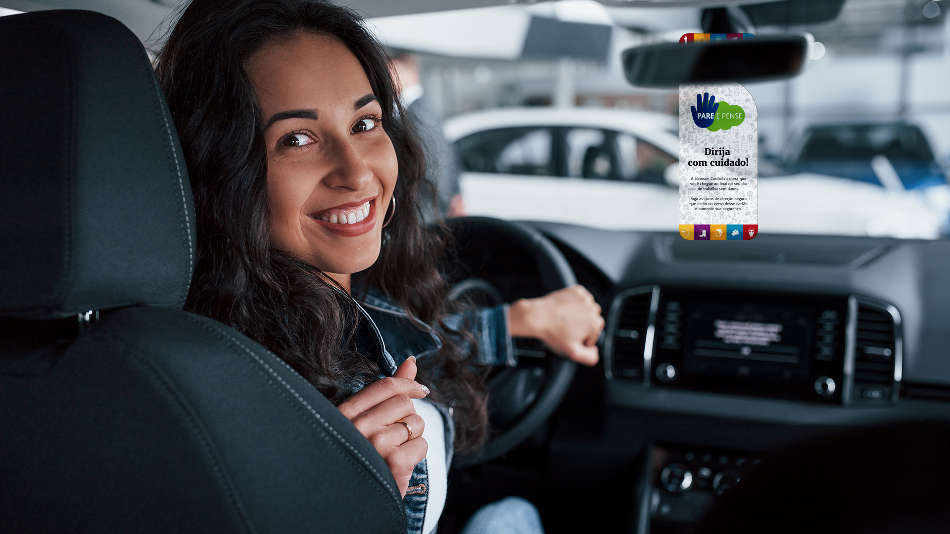 Imagem de moça sorrindo dentro de carro com tag no retrovisor com a comunicação da campanha de endomarketing Pare & Pense Johnson Controls.